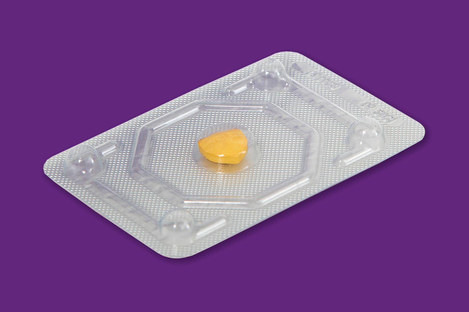 Comprimé jaune sous plaquette plastique alvéolée transparente sur fond violet.