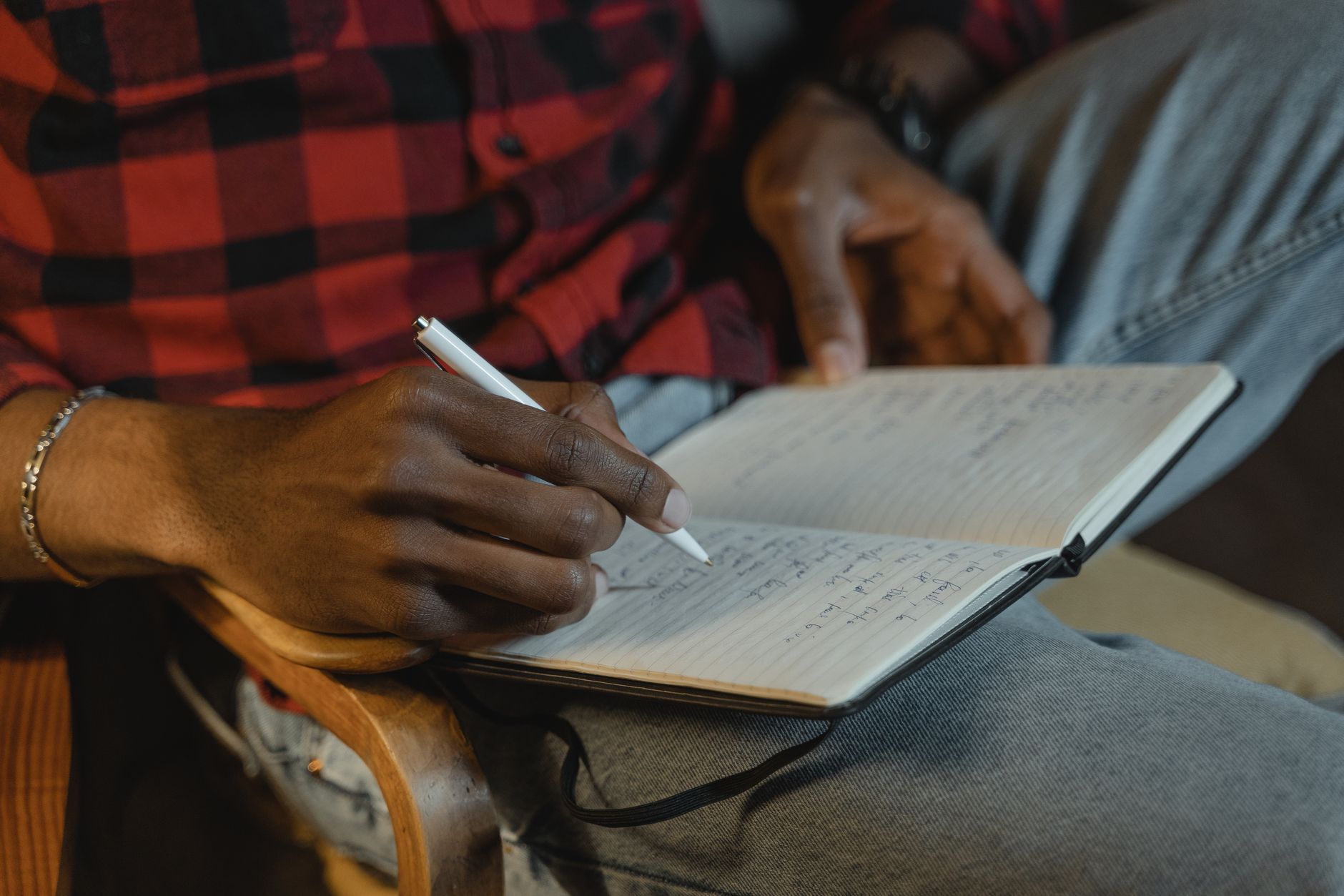 Gros plan sur les mains d’une personne écrivant au stylo dans un carnet ouvert.