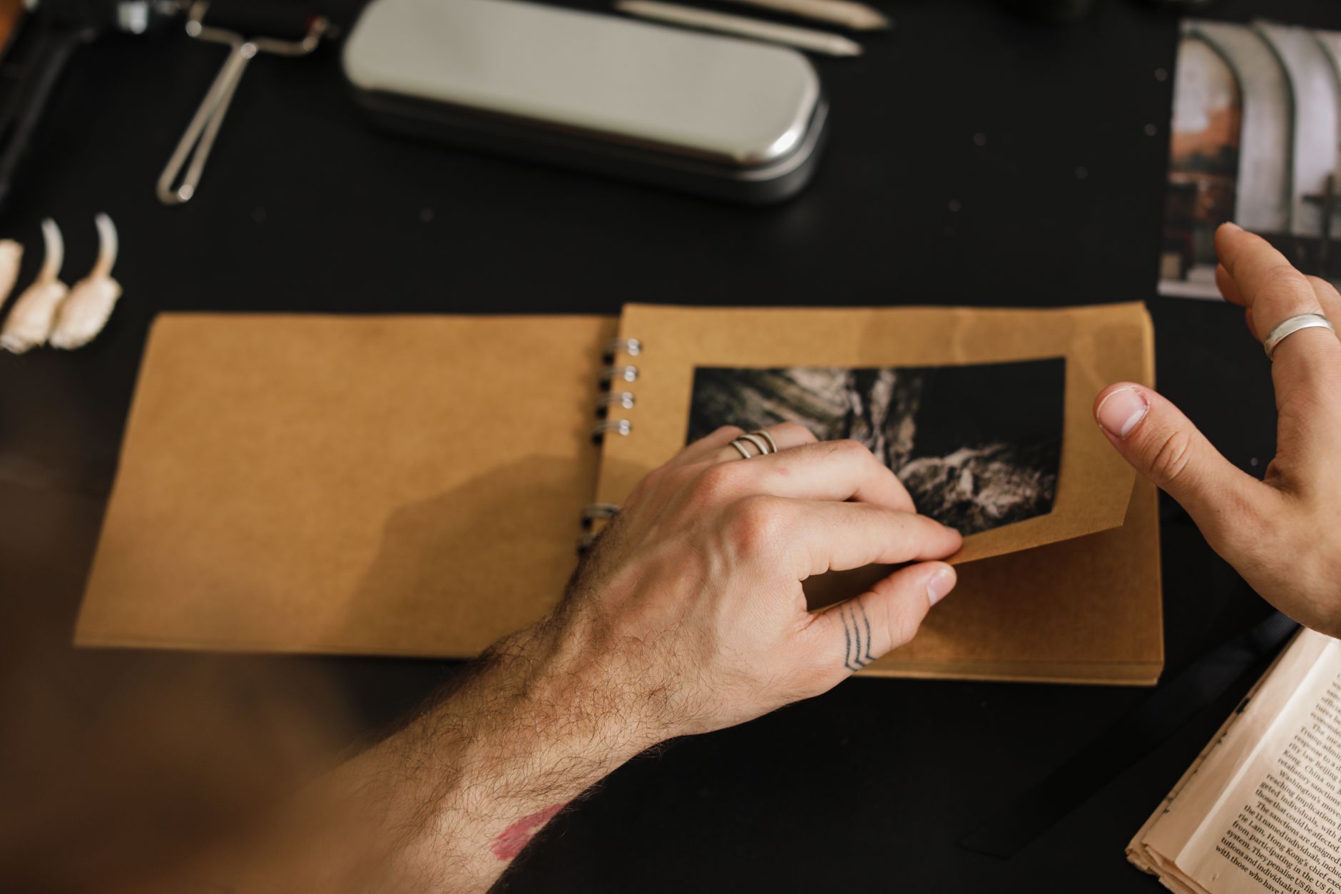 Mains feuilletant un album photo à spirale en papier kraft, avec une photographie en noir et blanc, sur une table sombre.